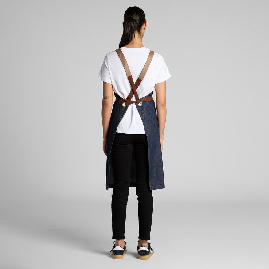 Person wearing a white shirt, black pants, and a blue apron with suspenders on a gray background