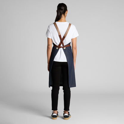 Person wearing a white shirt, black pants, and a blue apron with suspenders on a gray background