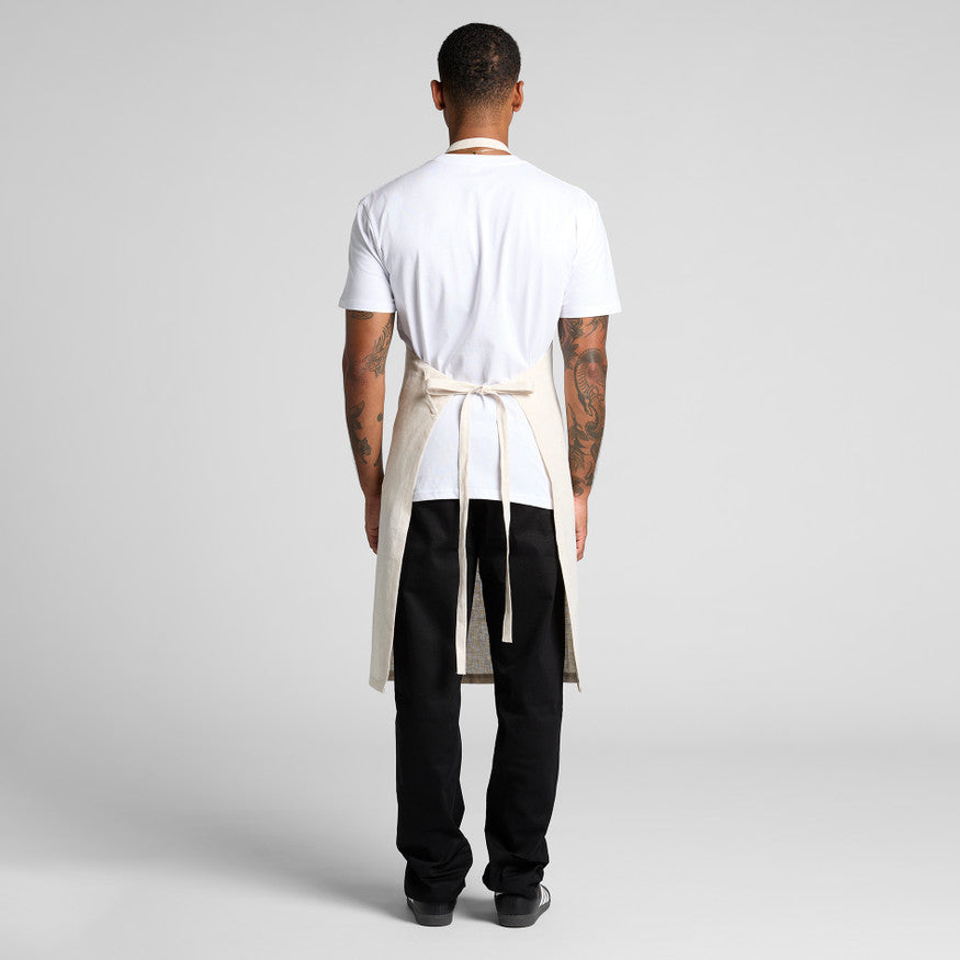 Person wearing a white shirt, black pants, and a beige apron on a plain background
