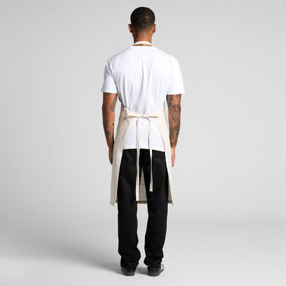 Person wearing a white shirt, black pants, and a beige apron on a plain background