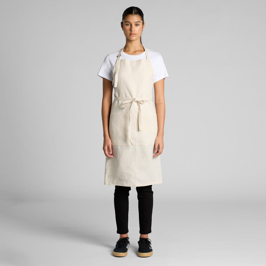 Person wearing a beige apron over a white shirt and black pants on a gray background