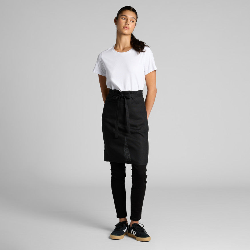 Person wearing a black apron over a white shirt on a gray background