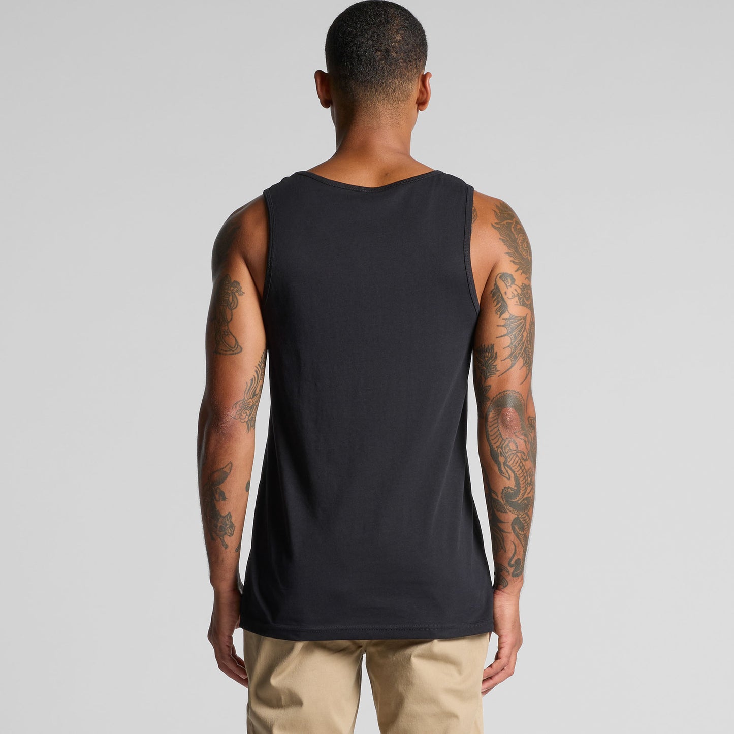 Man wearing a black tank top with visible tattoos on a gray background